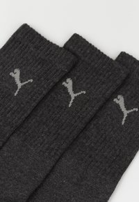Calcetines negros acanalados hechos de una tela suave, con un logo gris de Puma en el costado, presentados en una vista en primer plano.