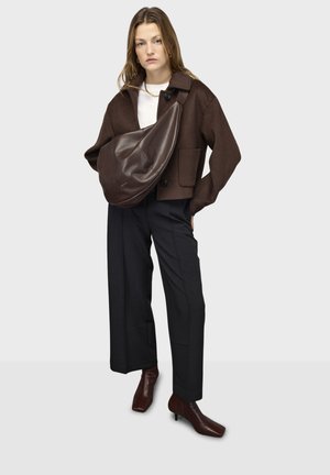 Giacca corta in misto lana marrone, camicia bianca, pantaloni neri su misura e borsa a tracolla in pelle marrone. Stivali alla caviglia con tacco a stiletto.