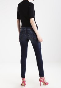Vaqueros ajustados de denim azul oscuro, con bolsillos traseros y costuras sutiles. Combinados con una blusa negra de manga corta y sandalias de tacón alto rosas.