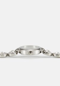 Orologio metallico con cassa rotonda in argento, quadrante trasparente e bracciale con accenti scintillanti simili a gioielli.