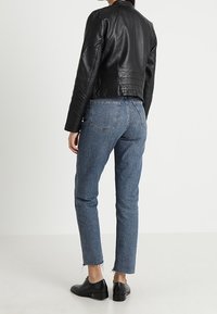 Černá kožená zkrácená bunda s přiléhavým střihem, v kombinaci s modrými džíny s vysokým pasem. Boty jsou černé, ploché s hladkým povrchem.