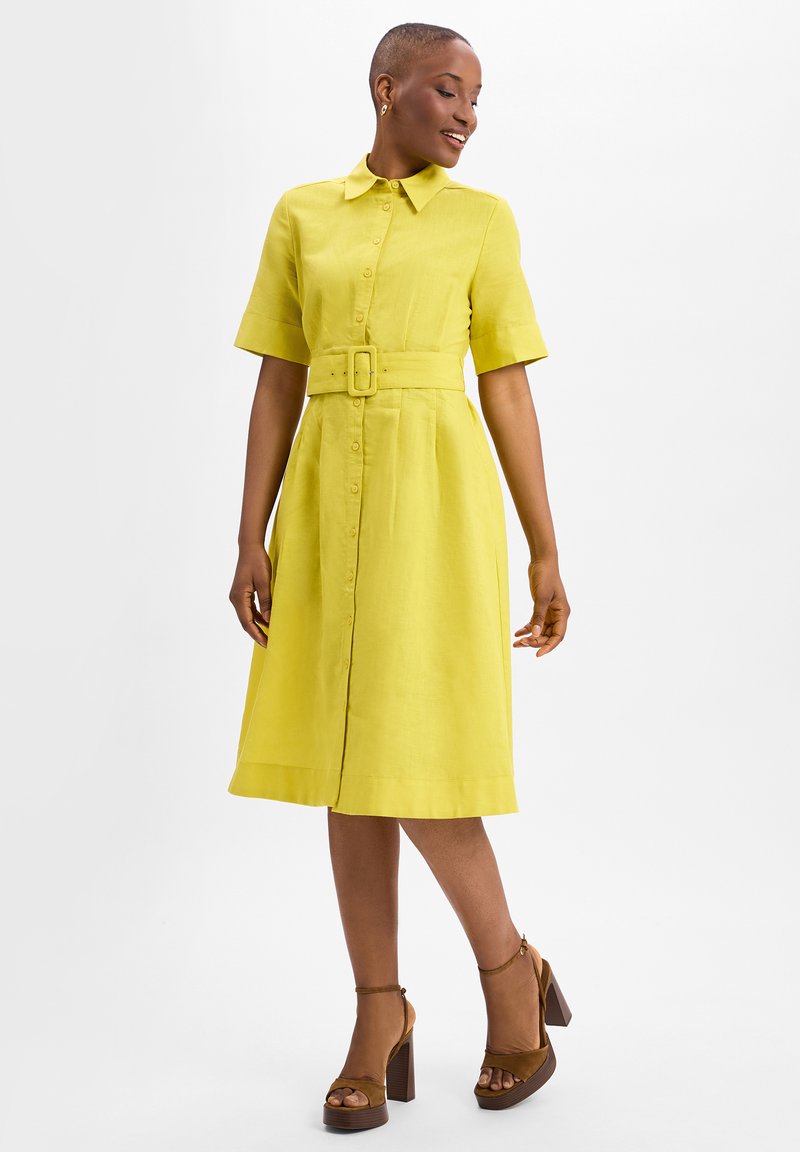 Linen shirt dress in bright yellow, featuring short sleeves, a belted waist, button front, and a flared hem, paired with brown platform shoes.