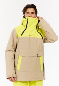 Beige en neon gele waterdichte jack met een hoge kraag, grote voorkant zak en zwarte ritssluitingen. Voorzien van een verstelbare kap.