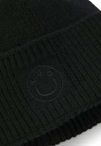 Czarna dziana czapka typu beanie z prążkowaną fakturą i subtelnym, haftowanym logo w kształcie uśmiechniętej buźki z przodu. Miękki, ciepły materiał.