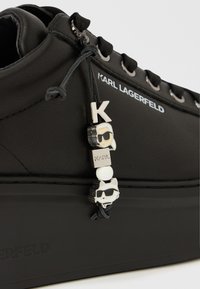 Μαύρο πλατφόρμα αθλητικό παπούτσι από λείο δέρμα, με μεταλλικά κορδόνια, μαύρα κορδ όνια και διακοσμητικό κρεμαστό με γράμματα και χαρακτήρα.