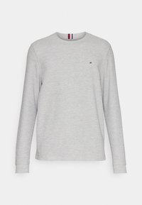 Harmaa pitkähihaisilla t-paita puuvillasekoitetta. Ominaisuuksia ovat pyöreä kaulus ja pieni logo punaisilla ja sinisillä yksityiskohdilla kauluksessa.