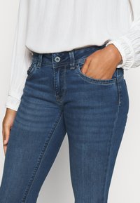 Blå denimjeans med slim fit, med knappstängning, bältesloopar och framfickor. Materialet verkar mjukt med subtila blekningar.