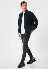 Svart denimjacka med dragkedja, elastiska ärmslut och två framfickor; matchad med svarta jeans och texturerade svarta sneakers.