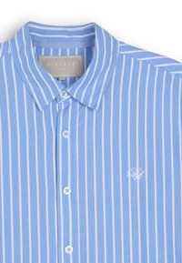 Jasnoniebieska koszula z guzikami, z białymi pionowymi paskami, kołnierzykiem i małym haftowanym logo. Materiał jest gładki z wyraźną teksturą.