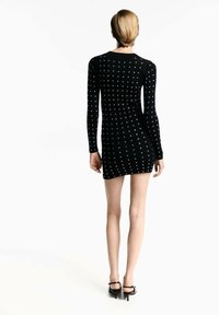 Abito nero a coste con maniche lunghe, decorato con pois bianchi. Ha una silhouette aderente, che raggiunge sopra la coscia, abbinato a tacchi alti.