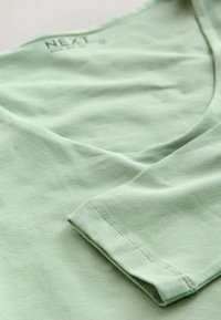 Lys grøn bomulds T-shirt med V-hals design og kortærmede. Glat tekstur med syningsdetaljer på ærmerne og halsudskæringen.