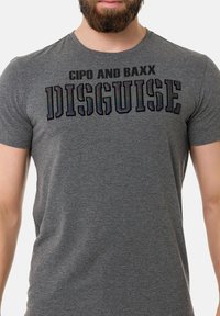 Graues Kurzarm-T-Shirt aus Baumwolle, mit auffälligem schwarzen Text "CIPO AND BAXX DISGUISE" in einer stilvollen Schriftart.