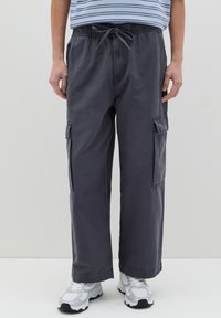 Pantaloni cargo grigi a gamba larga con vita regolabile, tasche laterali e una texture liscia, abbinati a sneaker bianche.