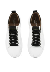 Sneakers in pelle bianca con lacci neri, texture liscia, design minimalista, accenti neri a contrasto e interno nocciola. Logo del brand visibile.