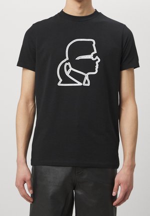 Mand iført sort T-shirt med korte ærmer med hvidt omrids grafik af en mands sideprofil iført solbriller og jakke med høj krave.