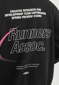 Sweatshirt noir avec du texte blanc et rose. Le design comprend les phrases "Runners Assoc." et une courbe graphique, fabriqué en tissu doux.
