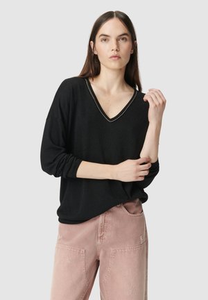 Maglione nero a V con una leggera lucentezza, caratterizzato da maniche lunghe e una vestibilità comoda, abbinato a jeans in denim rovinati di un delicato rosa chiaro.