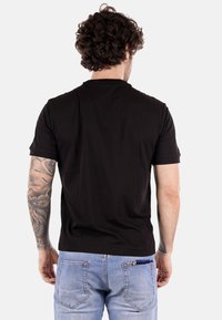 Camiseta negra de manga corta con cuello redondo, textura suave y corte relajado, combinada con jeans de mezclilla azul claro.