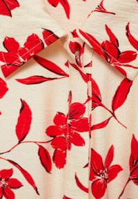 Rood bloempatronen shirt met een zachte stof, een kraaghalslijn en zichtbare stikseldetails op een licht crèmekleurige achtergrond.
