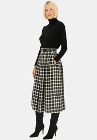 Czarny golf zestawiony z długą, wzorzystą w czarno-białą kratę spódnicą z kieszeniami i szerokim paskiem. Modelka ma na sobie czarne wysokie kozaki.