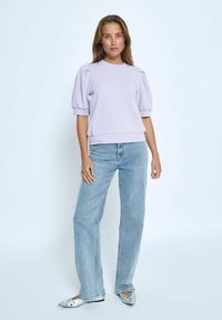 Lila sweatshirt med puffärmar, ribbad halsringning och nederkant, kombinerad med ljusblå raka jeans och mönstrade ballerinas.