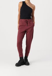 Bordeauxfärgade joggerbyxor med dragsko i midjan, smal passform och sidofickor; kombinerat med en svart ärmlös topp. Tjocka svarta stövlar fulländar looken.