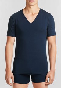 T-shirt blu navy a maniche corte con scollatura a V, realizzato in morbido cotone, con un design aderente e una superficie liscia. Indossato con pantaloni corti abbinati.