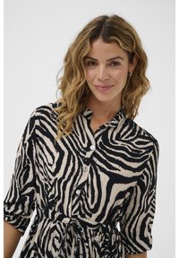 Zebramönstrad klänning i lätt tyg, med svarta och beige färger, en knapp-up krage, uppvikt ärm och en knytning i midjan.