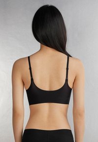 Černý bezšvový bralet s nastavovacími ramínky, hladkým povrchem a zakulaceným zadním designem, nabízející minimalistický vzhled.