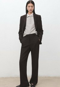 Ciemnobrązowy garnitur na miarę z szerokimi spodniami i jasnoszara polo z kołnierzykiem. Gładka tekstura, minimalistyczny design, brak widocznych wzorów.