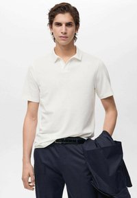 Wit polo shirt met korte mouwen en een klassieke kraag, gemaakt van een gladde stof, gecombineerd met donkere broek en een jasje over de arm.