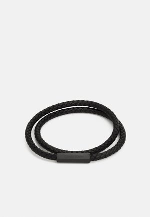 Bracciale in pelle intrecciata nera con una chiusura metallica rettangolare liscia che presenta il logo Calvin Klein. Due anelli per una vestibilità regolabile.