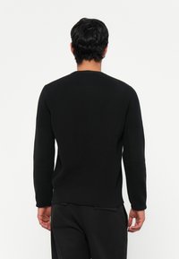 Pulover negru cu mâneci lungi, cu un model texturat de tricot, decolteu rotund și fante laterale, asortat cu pantaloni negri.