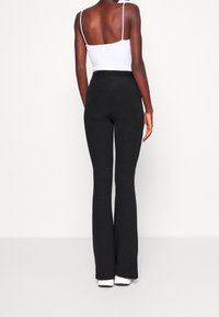 Černé rozšířené kalhoty z měkké látky s vysokým pasem a hladkým povrchem. Nošeny s bílým tílkem.