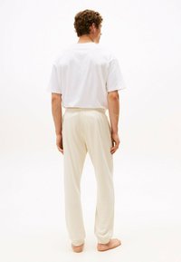 Camisa blanca de manga corta y pantalones beige con cinturilla elástica, vistos desde atrás. Tejido suave, corte relajado, diseño minimalista y sin estampados.