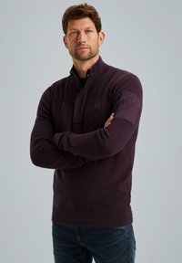 Dunkellila Pullover aus strukturiertem Stoff, mit einem Reißverschlusskragen, gerippten Bündchen und Saum sowie einem Logopatch auf dem linken Ärmel.
