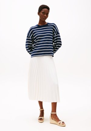 Pull à rayures bleu marine et blanc à manches longues, associé à une jupe midi plissée blanche et des sandales compensées beiges.