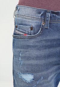 Niebieskie dżinsy z denimu z wyblakłym efektem, posiadające przetarcia, małą przednią kieszeń i widoczne detale przeszyć.