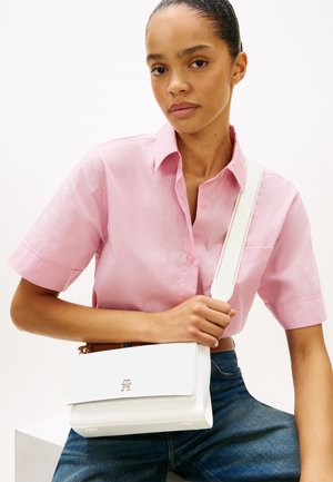 Sac à bandoulière en cuir blanc avec des ferrures dorées, une fermeture à rabat et une sangle amovible, posé sur un fond clair.