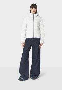 Hvid pufferjakke med quilted design og hætte, parret med vide ben i mørk denim. Jakken har en central lynlås og manchetter ved ærmerne.