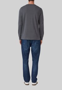 Graues Langarmshirt mit Rundhalsausschnitt, kombiniert mit blauen Jeans. Das Shirt hat eine glatte Textur; die Jeans verfügen über hintere Taschen.