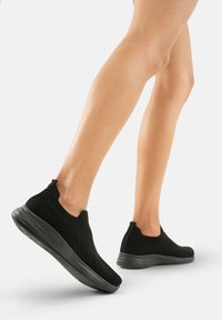 Schwarze Slipper-Sneaker mit einem strukturierten Strick-Obermaterial und einer flexiblen Sohle. Verfügt über ein niedriges Profil und minimal sichtbare Hardware.