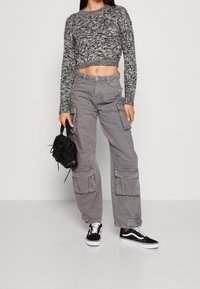 Grå kortärmad tröja med texturerad stickning, tillsammans med grå cargobyxor med flera fickor. Svarta sneakers och en liten svart handväska fulländar looken.