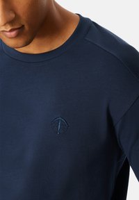 Marineblaues Sweatshirt mit Rundhalsausschnitt und gerippter Textur. Verfügt über ein dezentes gesticktes Logo auf der Brust. Glatte Stoffoberfläche.