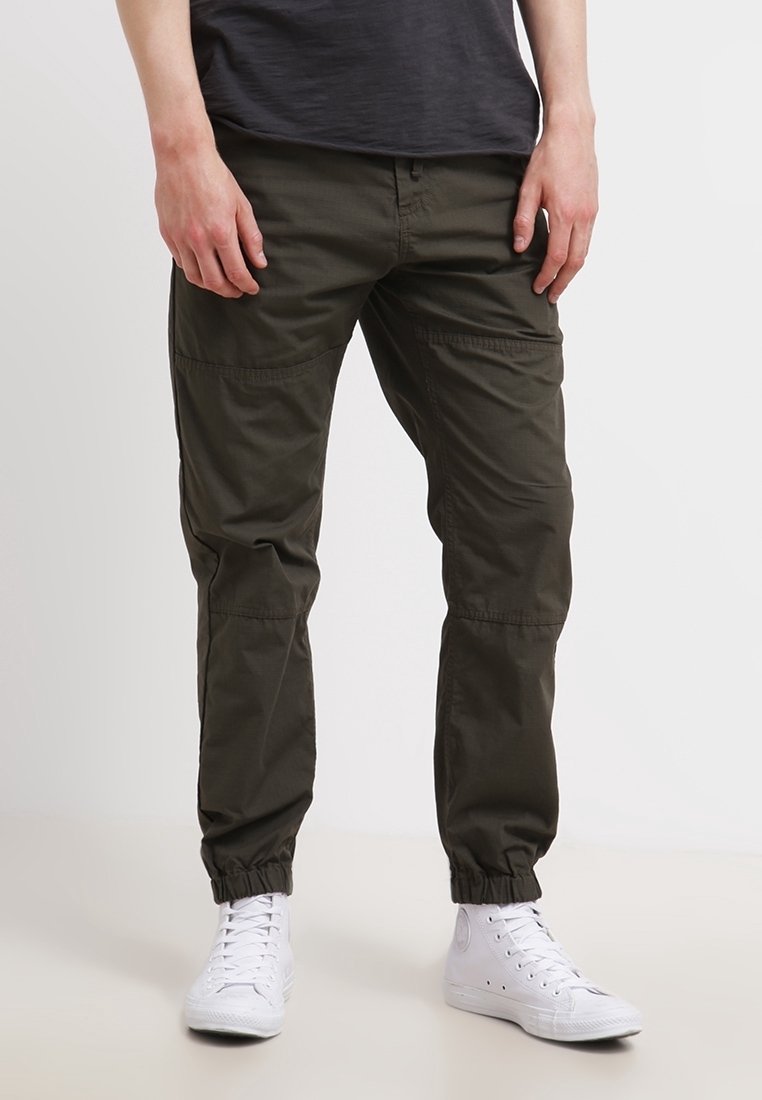 Oliven grønne cargobukser med elastiske manchetter, flere lommer og en afslappet pasform, kombineret med hvide høje sneakers.