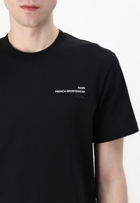 Czarna bawełniana koszulka z okrągłym dekoltem. Zawiera napis "PARIS FRENCH SPORTSWEAR" oraz małe czarne logo na lewej piersi.