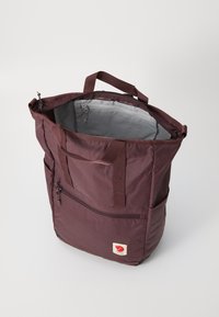 Bolso tote color burdeos con interior gris, que presenta dos asas superiores, un bolsillo con cremallera en la parte frontal y un parche con el logotipo. Fabricado en un tejido de nylon duradero.