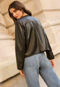 Veste en cuir noir avec un design court, des détails de couture visibles et des poignets boutonnés, associée à un jean taille haute bleu clair.