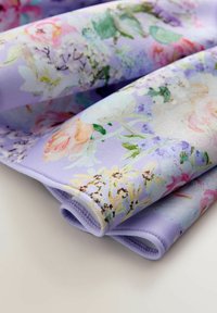 Sudėta levandų spalvos medžiaga su subtiliu gėlių raštu, kuriame yra rožinių, geltonų, žalių ir baltų gėlių ant lygaus paviršiaus.