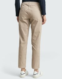 Beige Baumwollhosen mit lässiger Passform, ausgestattet mit Gesäßtaschen und umgeschlagenen Säumen. Gestylt mit weißen Sneakers und einem marineblauen Oberteil.
